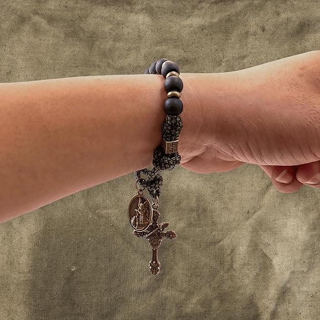 rosary with st michael medal on a wrist against a textured beige background