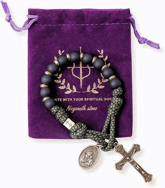 Black beaded one decade rosary with green accents and religious charms on a purple drawstring bag.